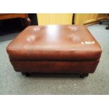 A brown faux leather footstool on castors,