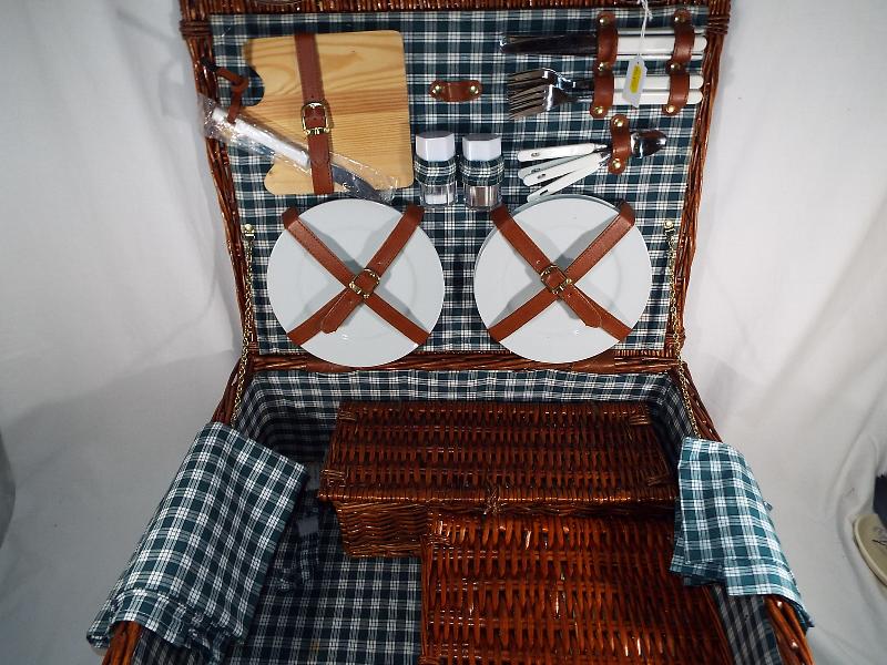 A good quality wicker picnic basket containing a 4 place setting to include ceramic plates, mugs,