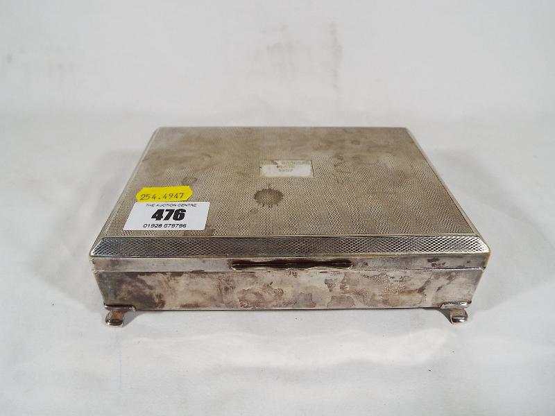 A silver plated cigar / cigarette box, engine turned decoration supported on four feet,