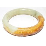 A hard stone carved a green jade and russet coloured  bangle depicting dragons chasing a silver