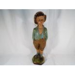 A ceramic figure depicting a young boy with hands in pockets,