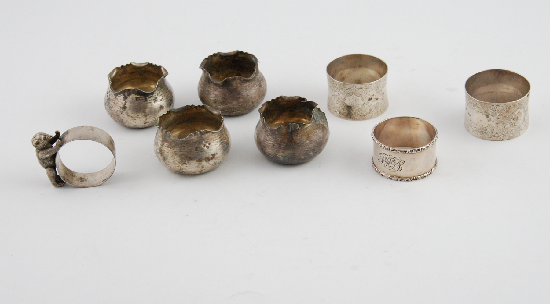 Set of four silver hammered salts with waved edges, 1884; a napkin ring with bear & three others,