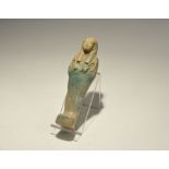 "20th century AD. An olive green glazed shabti with tripartite wig and agricultural implements in