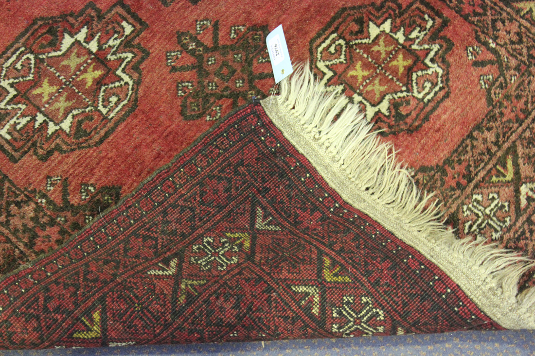 An Afghan rug, mid-20th Century, the claret field with two columns of five guls, within a - Image 2 of 2