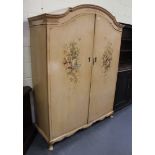 A 20th Century cream painted arched two-section wardrobe decorated with summer flowers, on