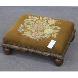 A late Victorian oak footstool, the needlework top above a carved oak leaf border, on turned legs,