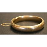 A gold oval hinged bangle on a snap clasp detailed '15', inside diameter approx 5.8cm, fitted with a