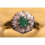 An 18ct gold, emerald and diamond cluster ring, claw set with the circular cut emerald within a