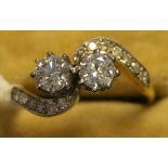 A gold and diamond two stone ring, claw set with the two principal diamonds in a crossover design,