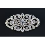 A platinum and diamond set brooch in a shaped oval scroll pierced panel design, mounted with the