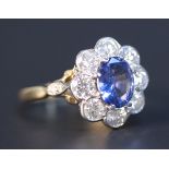A gold, sapphire and diamond oval cluster ring, claw set with the oval cut sapphire in a surround of