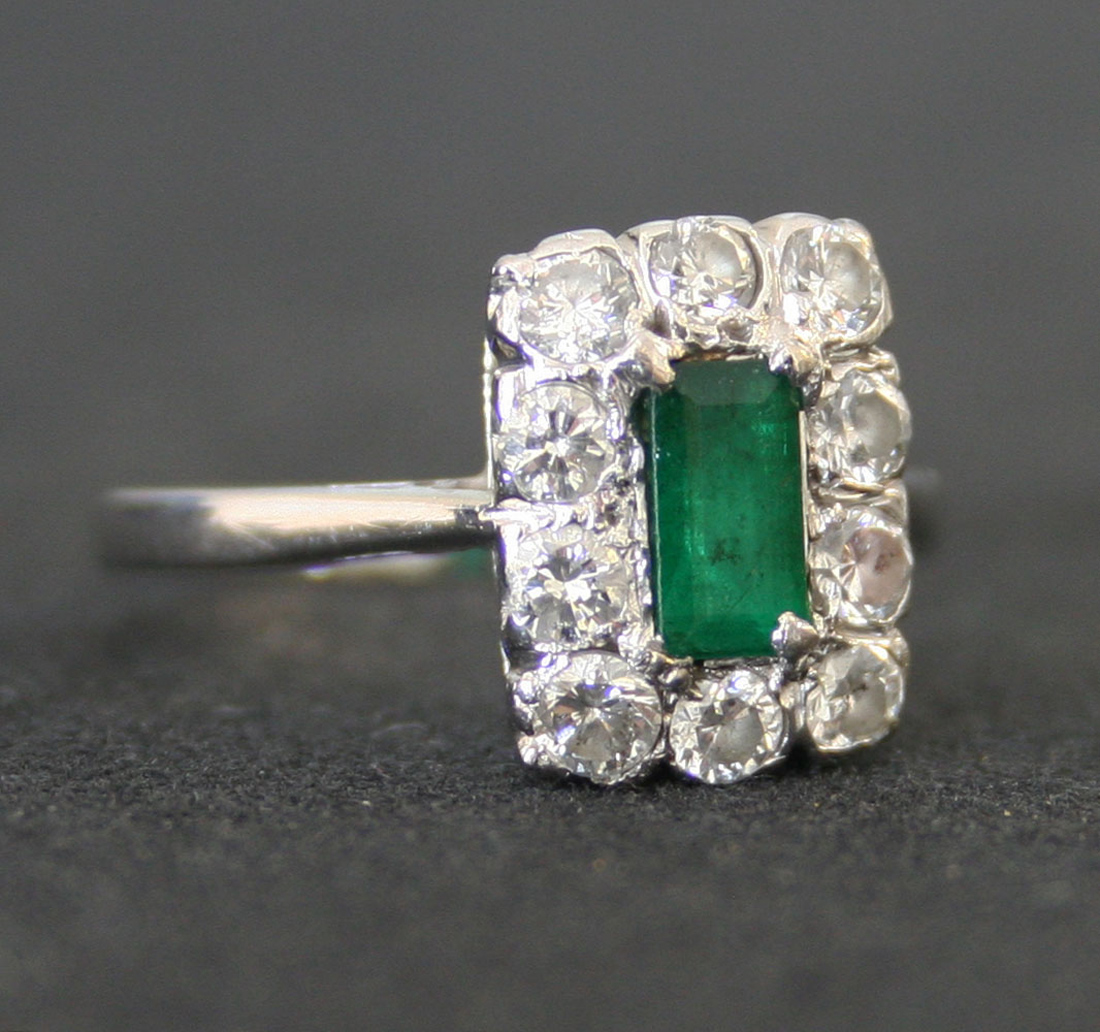 An 18ct white gold, emerald and diamond rectangular cluster ring, claw set with the rectangular step