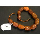 A single row necklace of twelve carved graduated semi-translucent vari-coloured dark honey