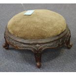 A Victorian walnut footstool, with an overstuffed top and a carved and shaped frame, on short carved