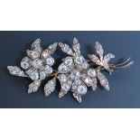 A diamond set brooch, designed as a floral and foliate spray, the two flowerheads mounted with