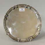 A George V silver circular salver with raised rim, on scroll legs terminating in hoof feet,