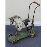 A late 19th Century painted pine push-along horse, the green painted base fitted with wheels, height