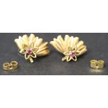 A pair of gold and ruby set single stone ear studs, each in a stylized floral and fanned design, the