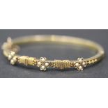 A gold and seed pearl set oval hinged bangle, the front with three quatrefoil shaped motifs,