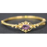 A gold, mauve gem and seed pearl set oval hinged bangle, circa 1910, collet set with the oval cut