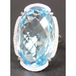 A blue topaz and diamond ring, claw set with the large oval cut blue topaz within a surround of