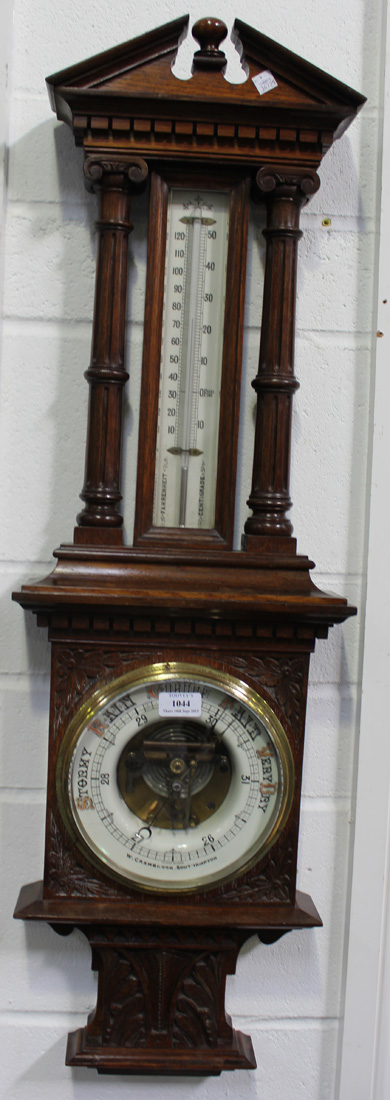 A late Victorian oak aneroid barometer with mercury thermometer, the ceramic circular dial inscribed