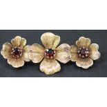 A 9ct gold and garnet set brooch, designed as a row of three flowerheads, each centre claw set