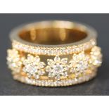 A gold and diamond band ring, designed as a row of five diamond set flowerheads between diamond