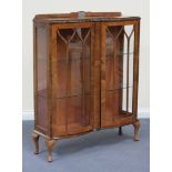 An early 20th Century walnut display cabinet, fitted with two glazed doors, raised on cabriole legs,