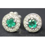 A pair of white gold, emerald and diamond set circular set studs, the backs with post and