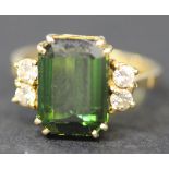 A gold ring, claw set with a rectangular cut tourmaline between two circular cut diamonds, ring size