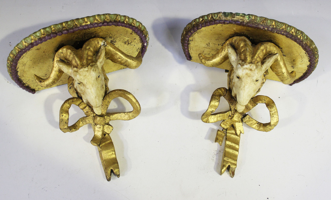 A pair of late 19th Century cream and gilt painted wall brackets, each with a ram's mask and tied