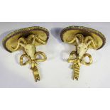 A pair of late 19th Century cream and gilt painted wall brackets, each with a ram's mask and tied