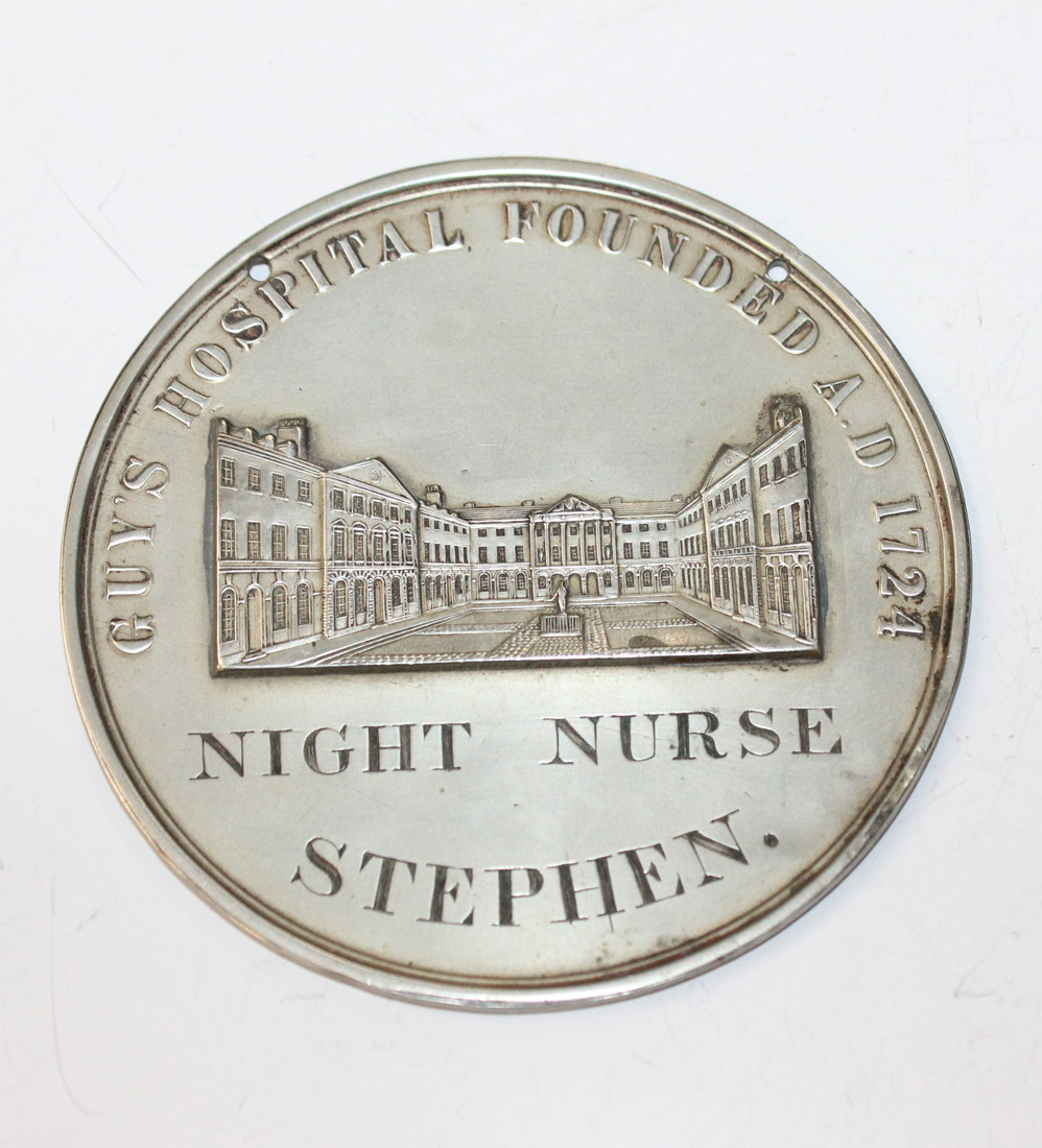 A circular white metal medallion or pass, detailed 'Guy's Hospital, Founded AD1724' above a relief