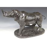 A 20th Century black patinated cast bronze figure of a rhinoceros, standing on an oval base,