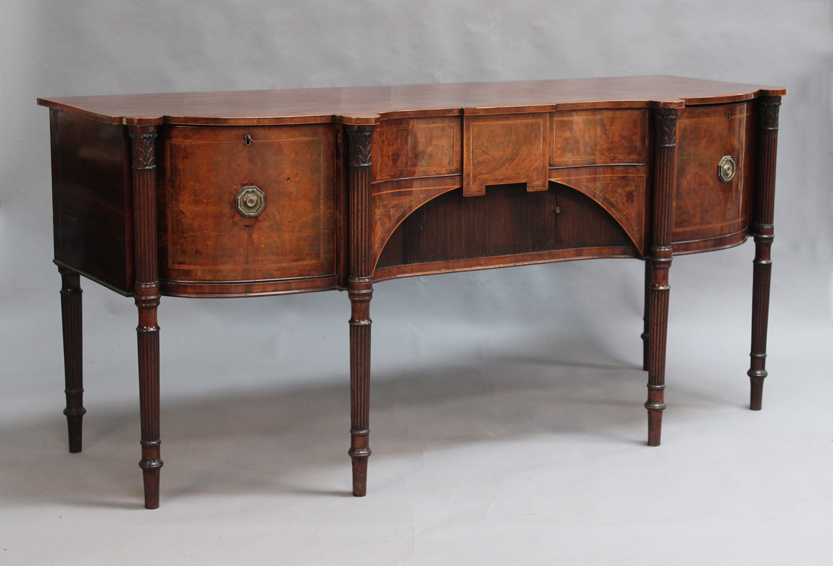 A George III figured mahogany and rosewood crossbanded sideboard, the shaped top with four