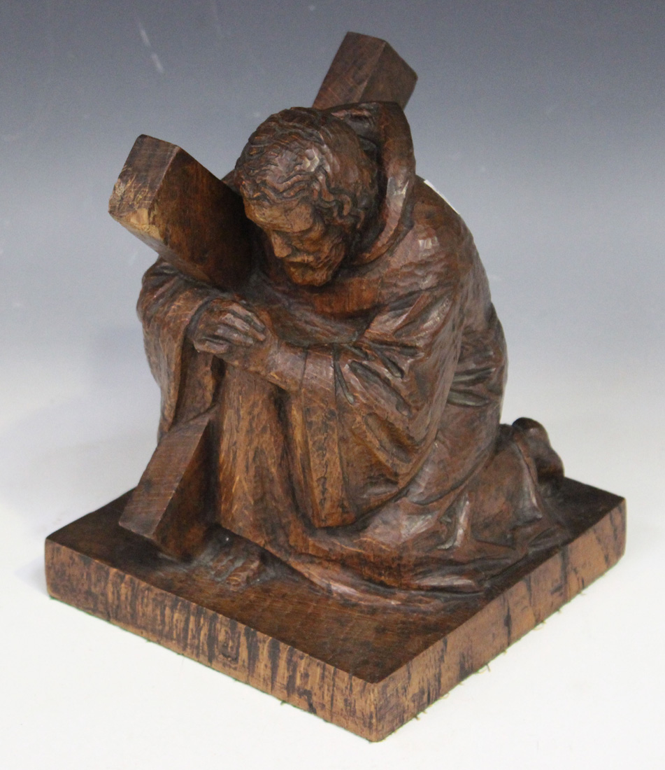 A 20th Century carved oak figure of St Andrew, praying on one knee and supporting an X-shaped cross,