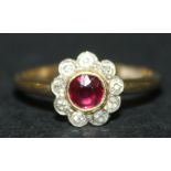 A gold, ruby and diamond set cluster ring, mounted with the cushion shaped ruby in a surround of