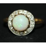 A gold and platinum, opal and diamond cluster ring, claw set with the circular opal within a