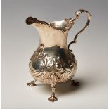 A Victorian silver cream jug with foliate capped scroll handle, the baluster body chased with