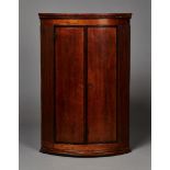 A George III oak bowfront hanging corner cabinet, fitted with a pair of mahogany crossbanded