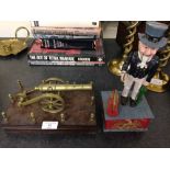 A brass model cannon on a wooden plinth with a reproduction cast iron Uncle Sam money box.