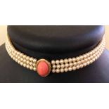 Faux pearl choker necklace with 3 strings of small faux pearls and a central oval coral coloured