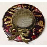A brooch in the form of a wide brimmed hat with red & gold enamelling.