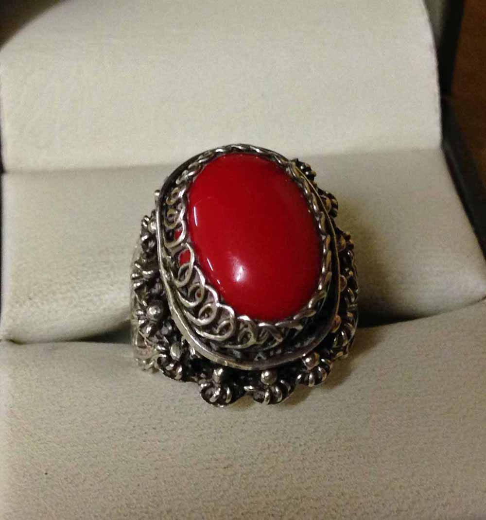 A white metal Egyptian 'poison' ring set with red oval cabouchon stone above poison compartment.