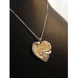 A silver heart shaped 'footsteps' pendant with gold highlights, on a silver chain.