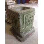 A square concrete garden planter with flower decoration, approx 45cm tall and 32cm square.