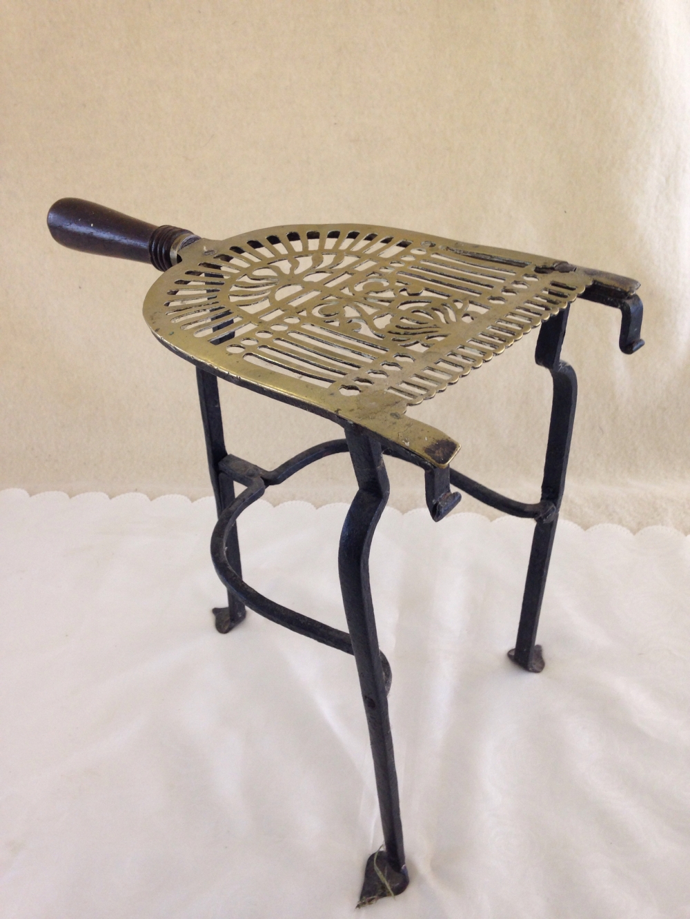 A brass trivet with cast iron legs and wooden handle.