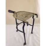 A brass trivet with cast iron legs and wooden handle.