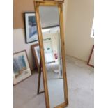 A gold coloured full length floor standing mirror.